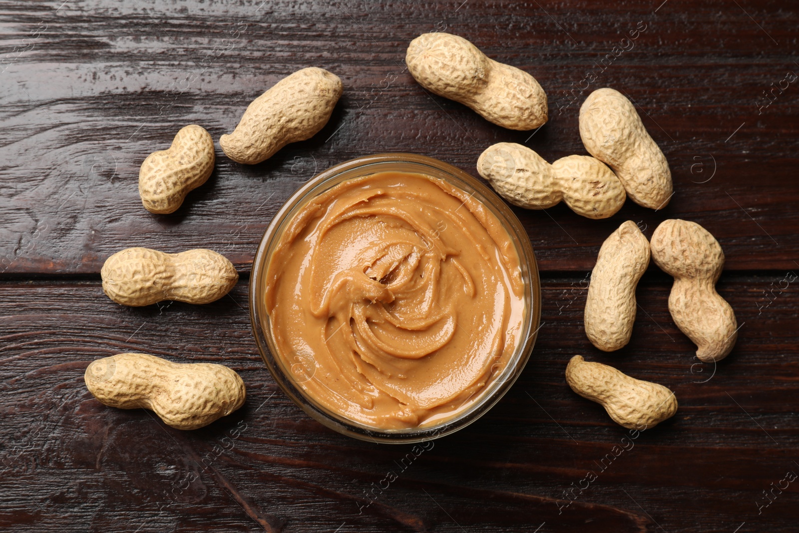 Photo of Tasty peanut butter in bowl and nuts on wooden table, flat lay