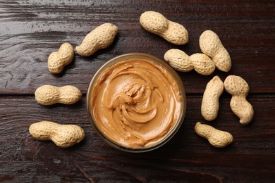 Photo of Tasty peanut butter in bowl and nuts on wooden table, flat lay