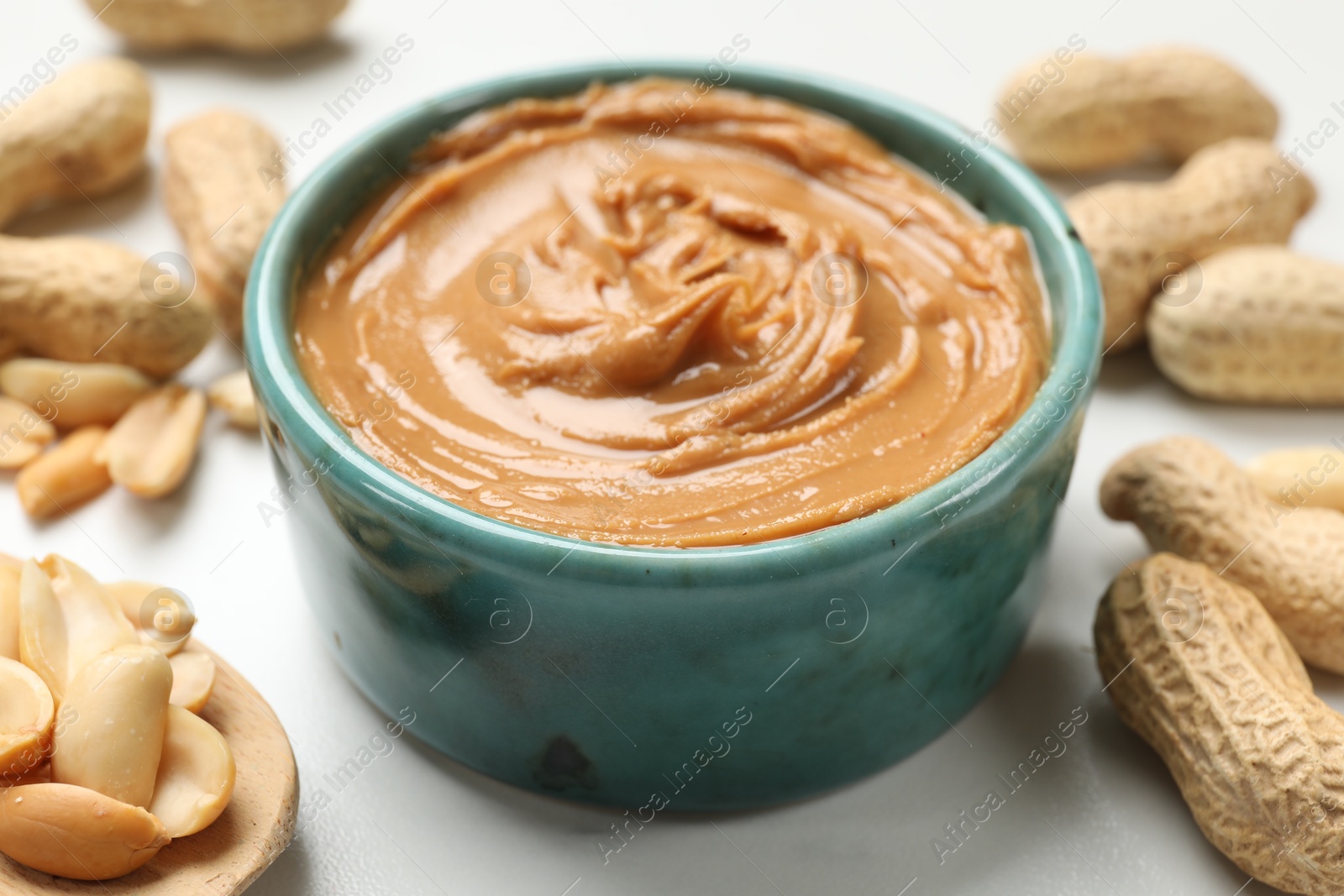 Photo of Tasty peanut butter in bowl and groundnuts on white table, closeup