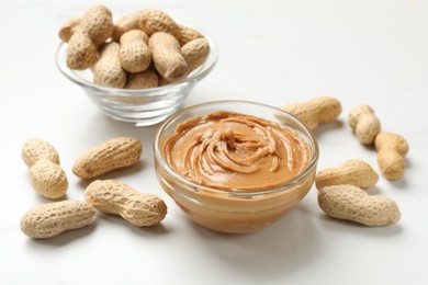 Photo of Tasty peanut butter in bowls and groundnuts on white table, closeup