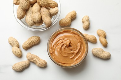 Photo of Tasty peanut butter in bowls and groundnuts on white table, flat lay