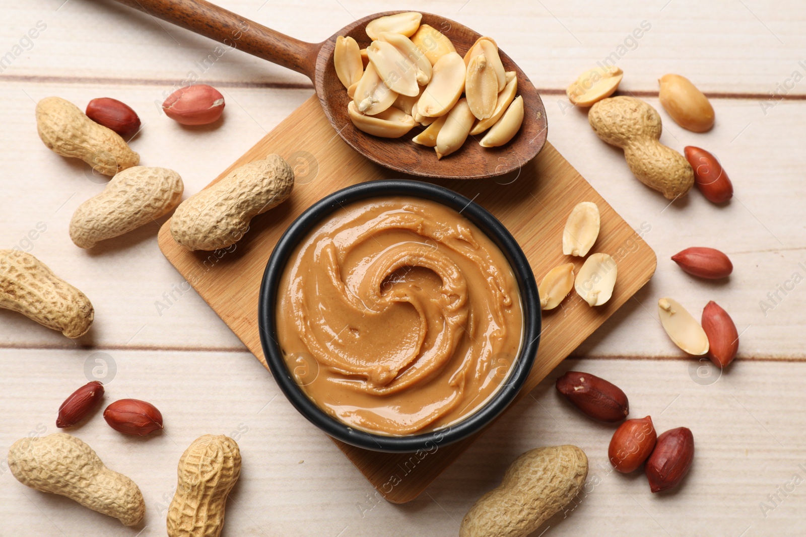 Photo of Tasty peanut butter in bowl and nuts on wooden table, flat lay