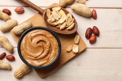 Photo of Tasty peanut butter in bowl and nuts on wooden table, flat lay