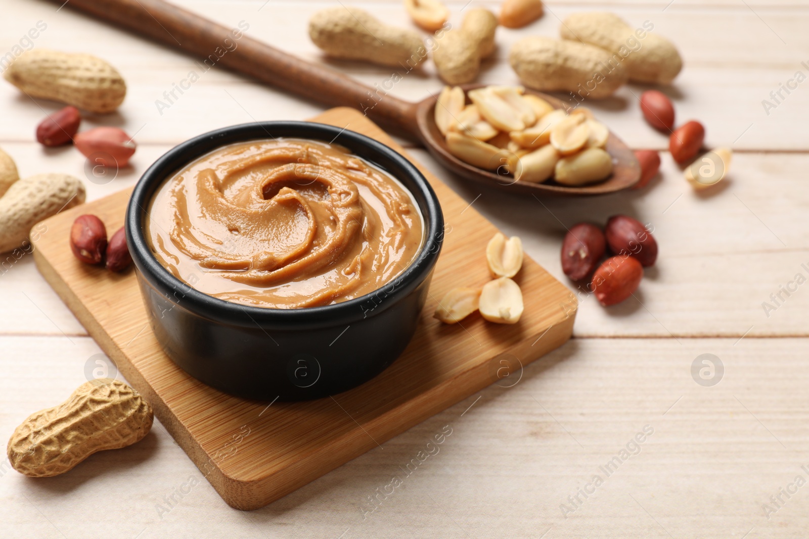 Photo of Tasty peanut butter in bowl and spoon with groundnuts on wooden table, closeup