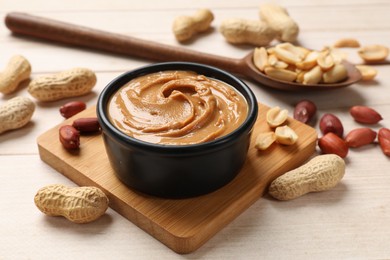 Photo of Tasty peanut butter in bowl and spoon with groundnuts on wooden table, closeup