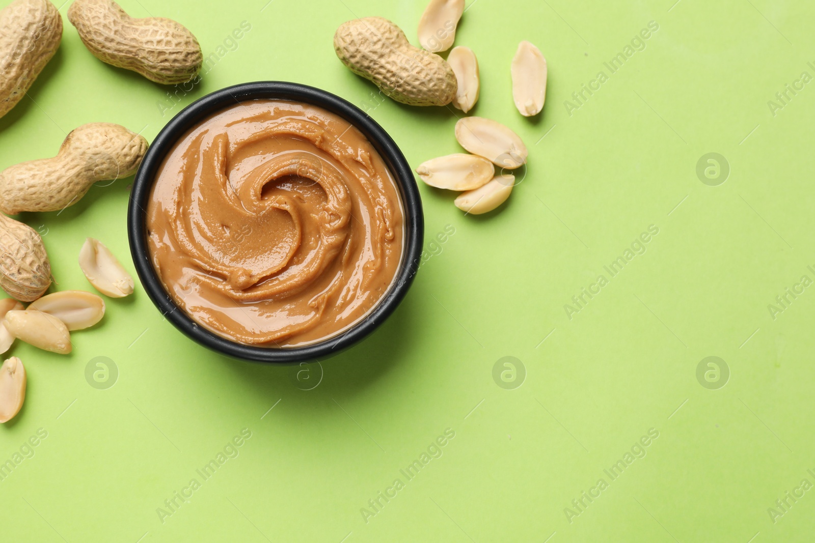 Photo of Tasty peanut butter in bowl and groundnuts on green table, flat lay. Space for text