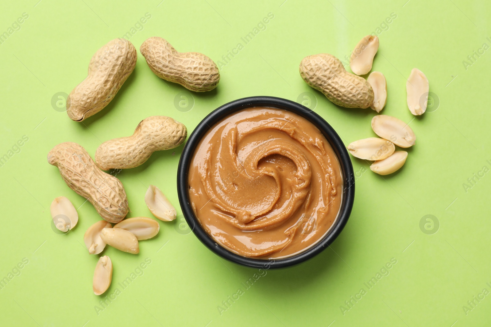 Photo of Tasty peanut butter in bowl and groundnuts on green table, flat lay