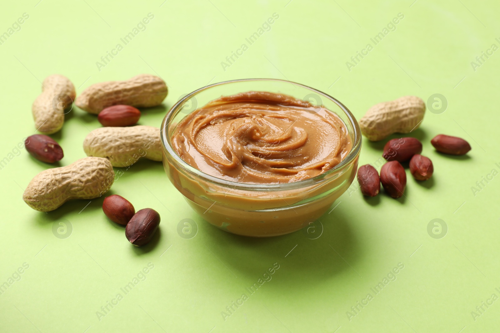 Photo of Tasty peanut butter in bowl and groundnuts on green table