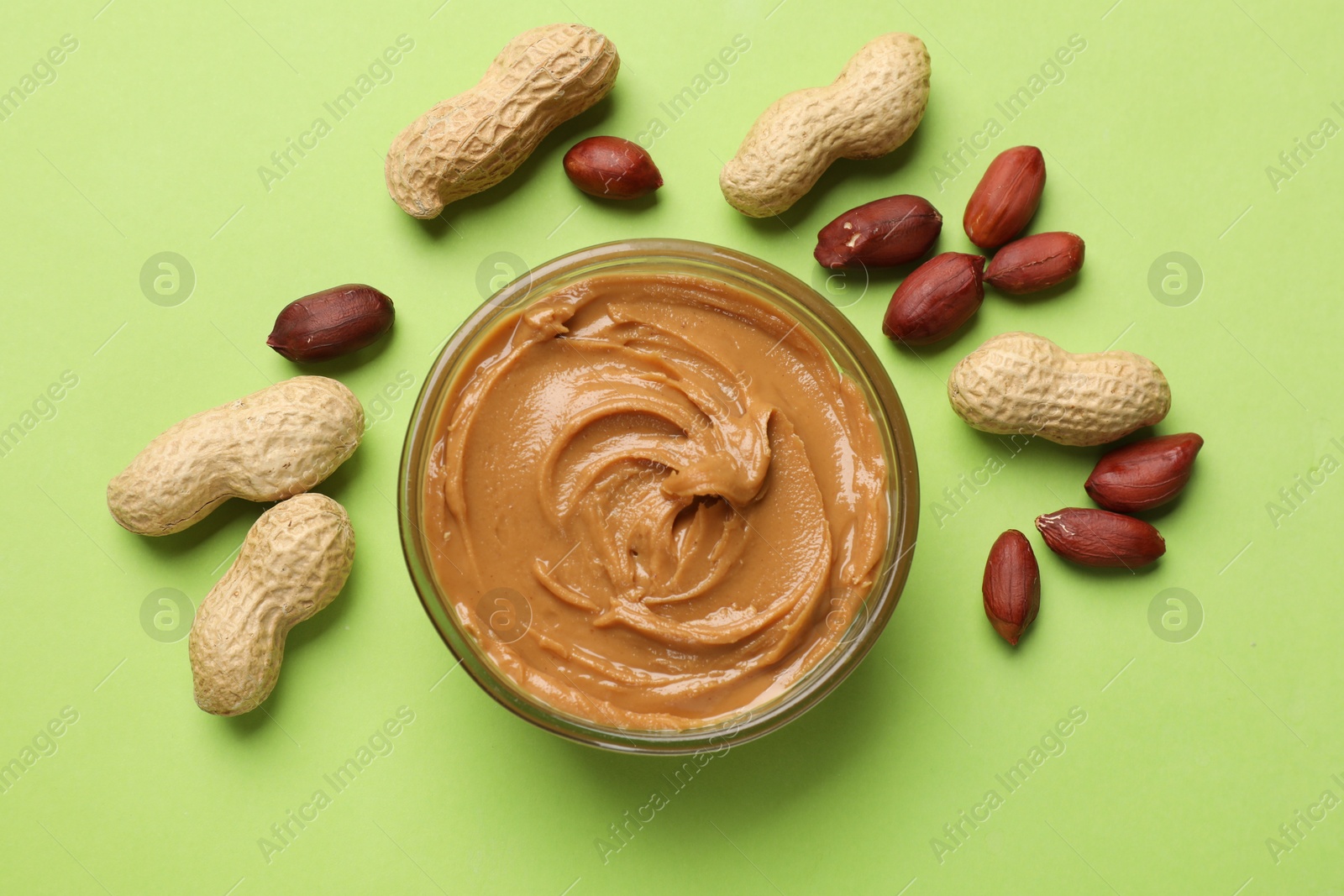 Photo of Tasty peanut butter in bowl and groundnuts on green table, flat lay