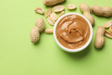 Tasty peanut butter in bowl and groundnuts on green table, flat lay. Space for text