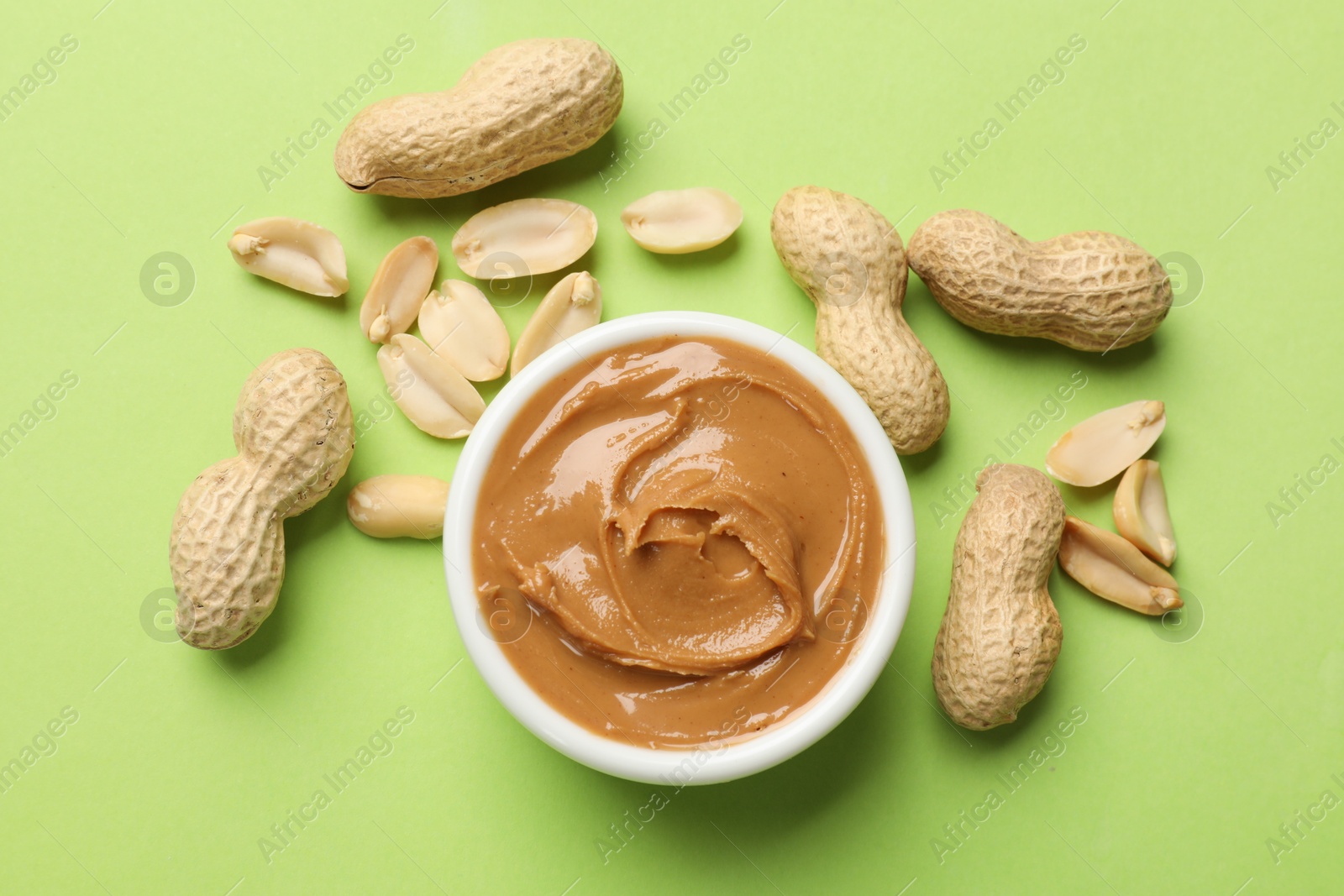 Photo of Tasty peanut butter in bowl and groundnuts on green table, flat lay