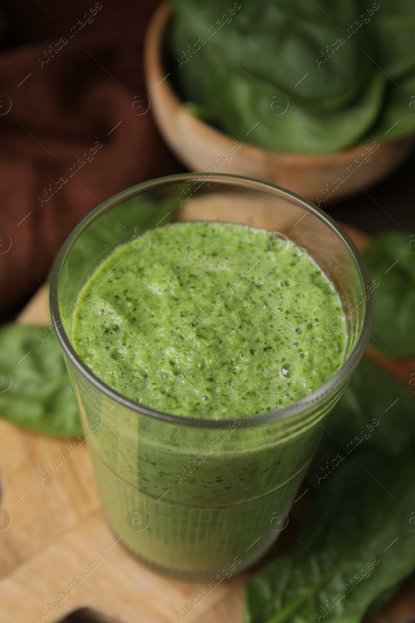 Photo of Tasty green smoothie in glass and spinach on table, closeup