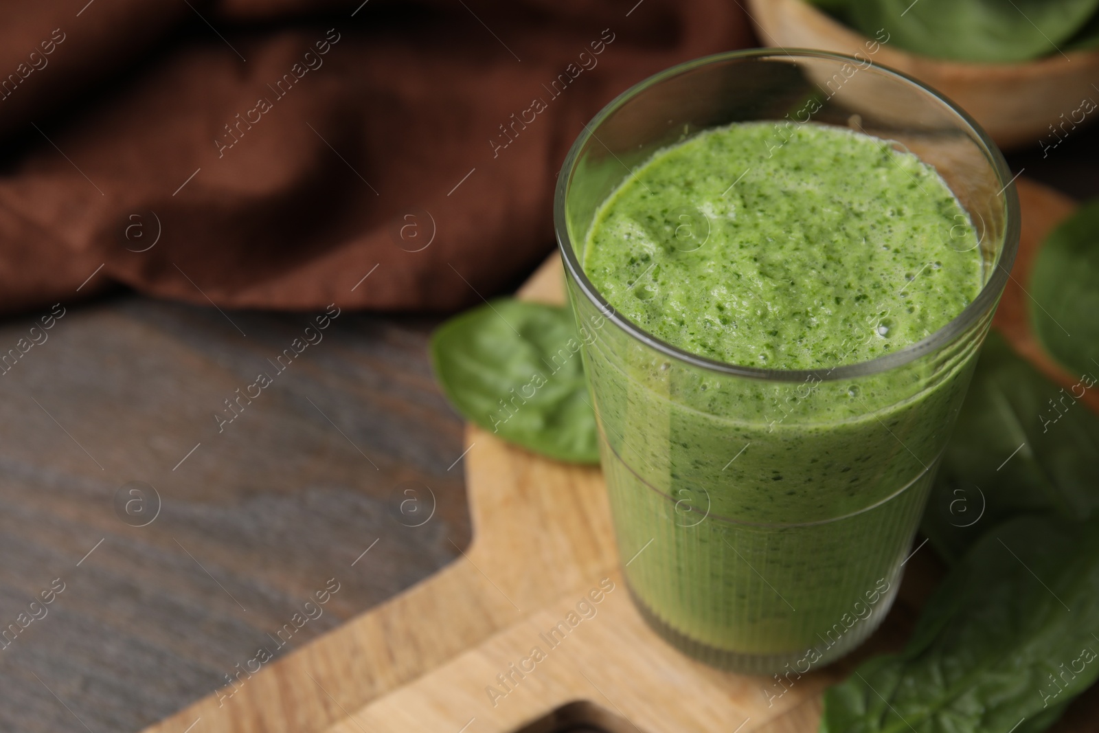 Photo of Tasty green smoothie in glass and spinach on wooden table, closeup. Space for text