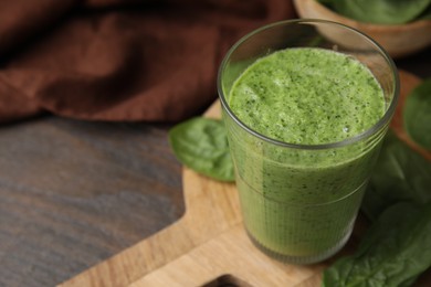 Photo of Tasty green smoothie in glass and spinach on wooden table, closeup. Space for text