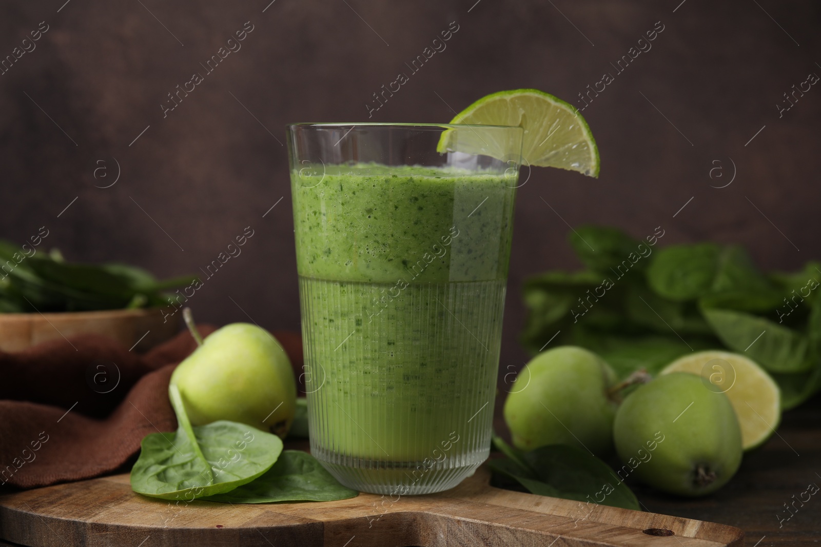 Photo of Tasty green smoothie in glass with lime, apples and spinach on wooden table, closeup