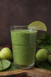 Photo of Tasty green smoothie in glass with lime, apples and spinach on table, closeup