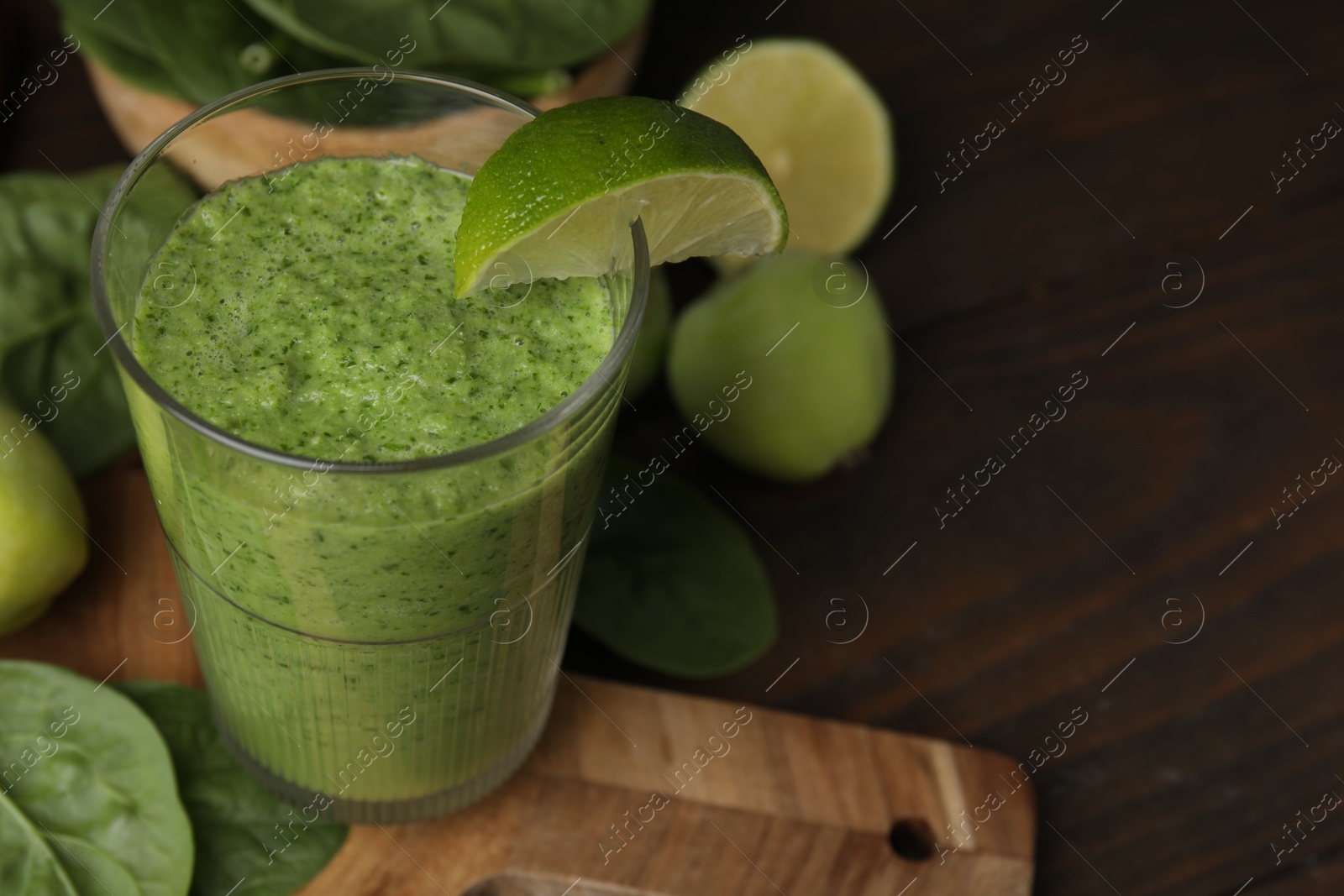 Photo of Tasty green smoothie in glass with lime, apples and spinach on wooden table, closeup. Space for text