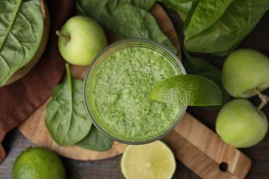 Photo of Tasty green smoothie in glass with lime, apples and spinach on wooden table, flat lay