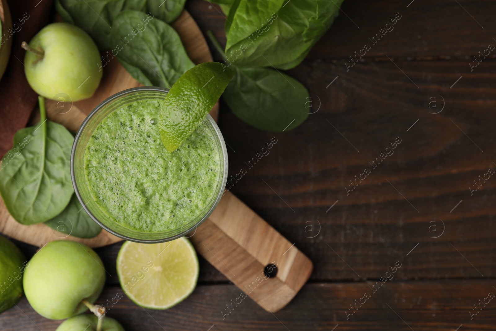 Photo of Tasty green smoothie in glass with lime, apples and spinach on wooden table, flat lay. Space for text