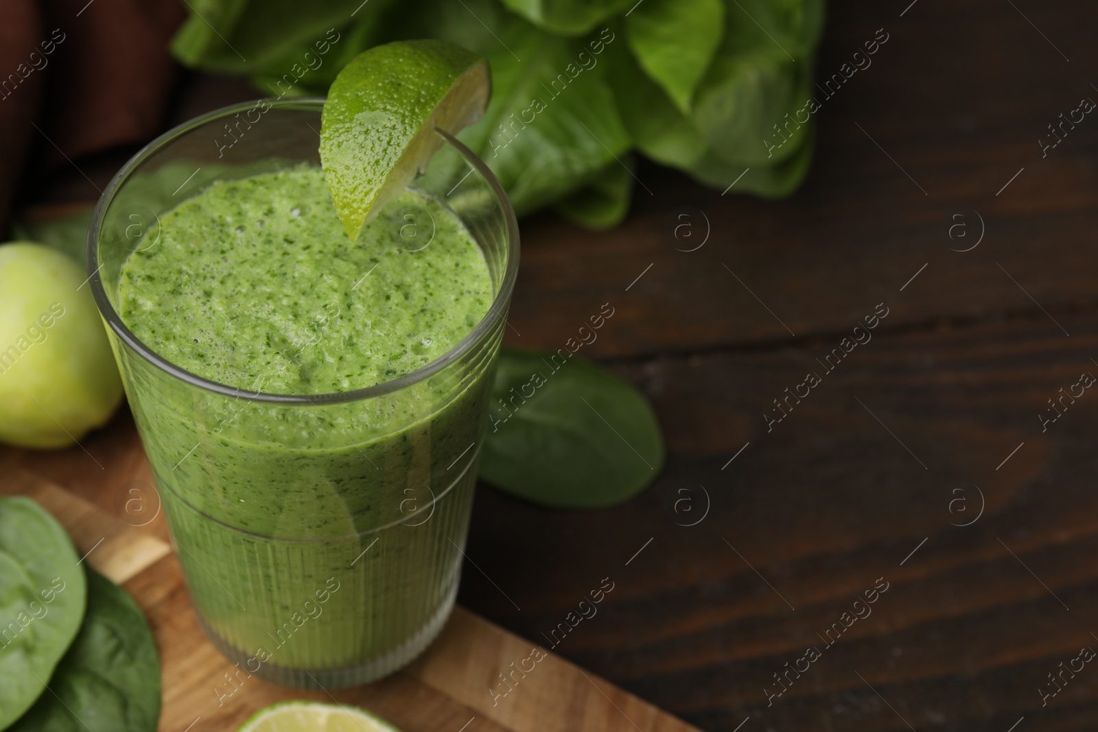 Photo of Tasty green smoothie in glass with lime on wooden table, closeup. Space for text