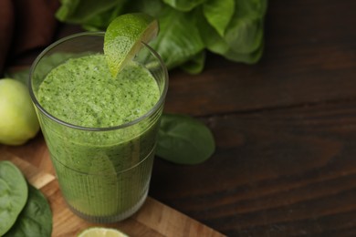 Photo of Tasty green smoothie in glass with lime on wooden table, closeup. Space for text