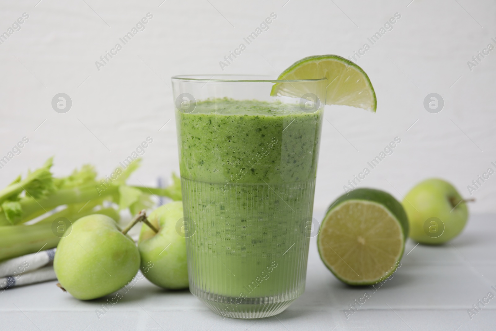 Photo of Tasty green smoothie in glass with lime and apples on white tiled table, closeup