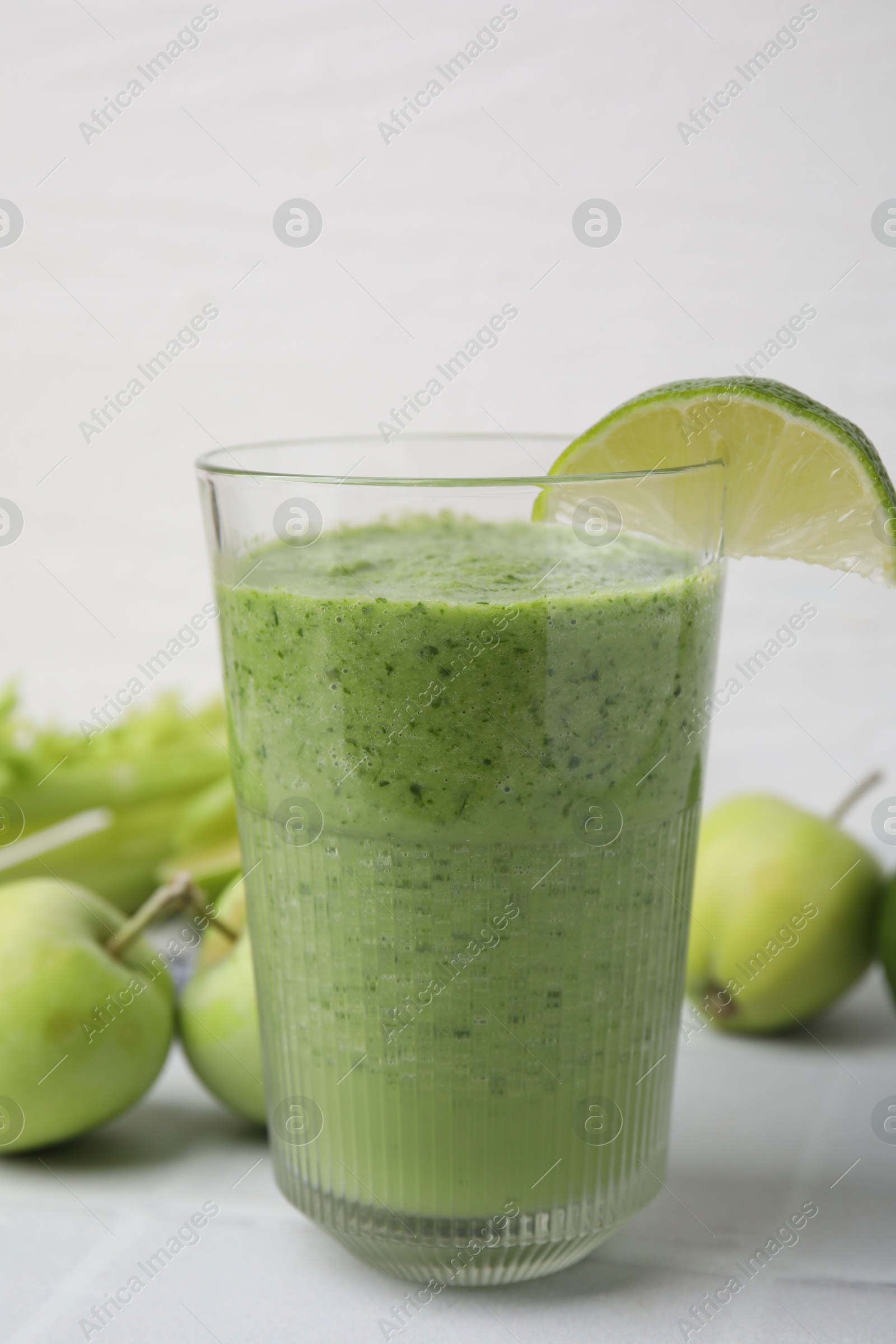 Photo of Tasty green smoothie in glass with lime and apples on white tiled table, closeup