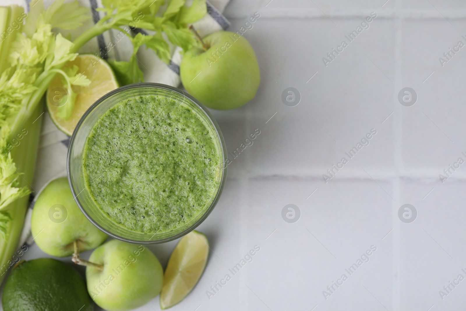 Photo of Tasty green smoothie in glass, lime, celery and apples on white tiled table, flat lay. Space for text