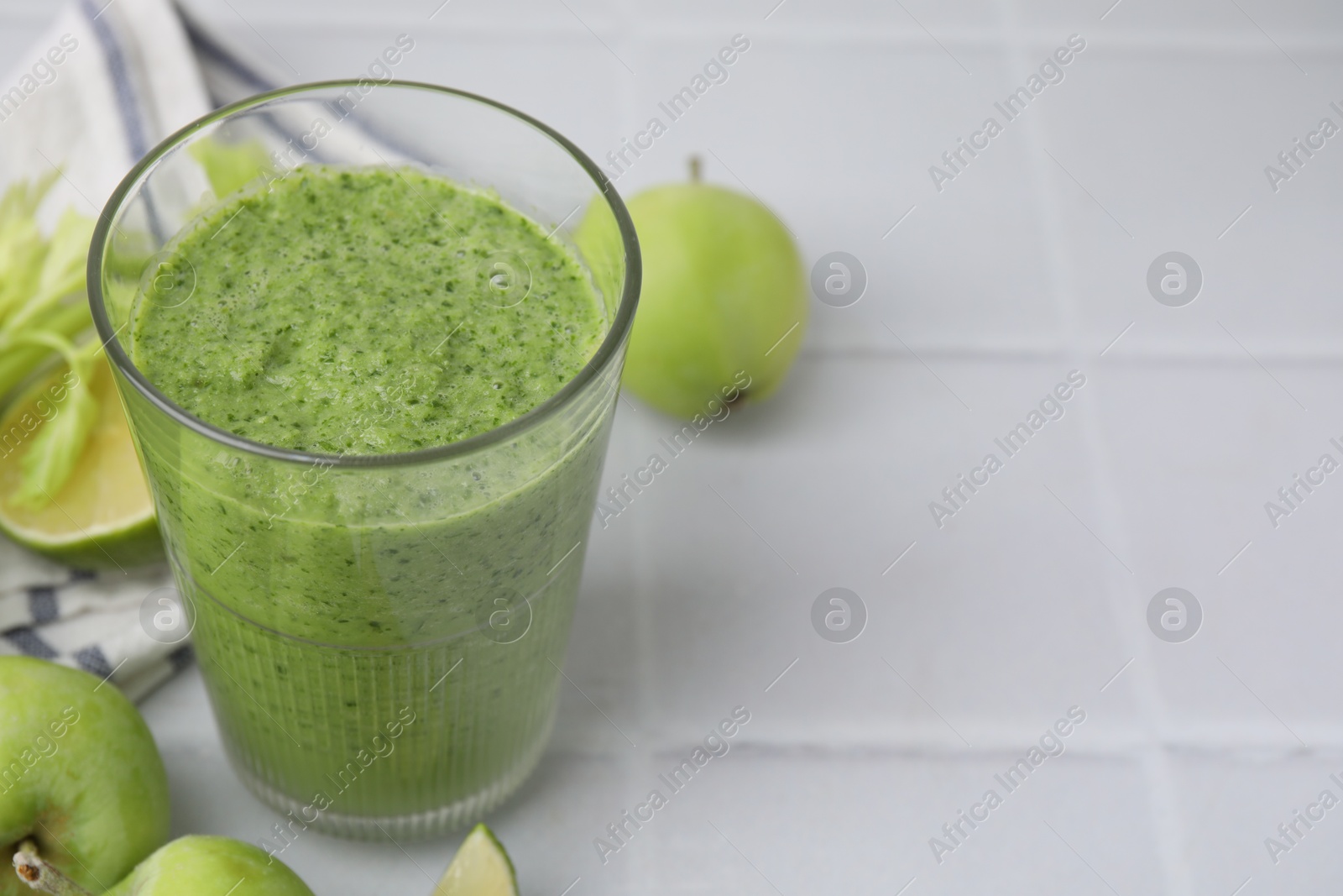 Photo of Tasty green smoothie in glass and apples on white tiled table, closeup. Space for text