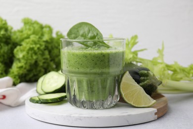 Photo of Tasty green smoothie in glass, lime and vegetables on light table, closeup