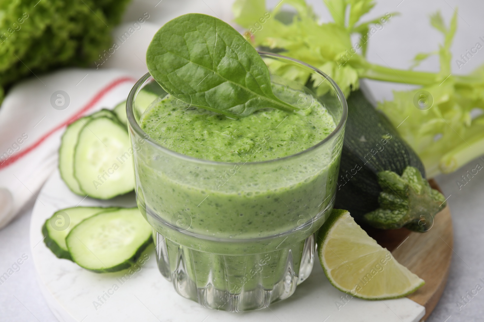 Photo of Tasty green smoothie in glass, lime and vegetables on light table, closeup