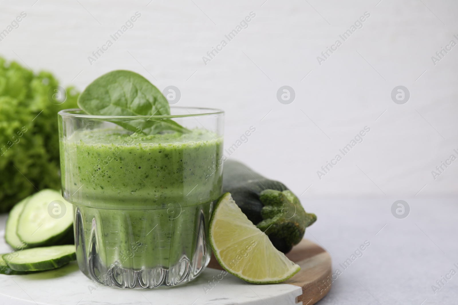 Photo of Tasty green smoothie in glass, lime and vegetables on light table, closeup. Space for text