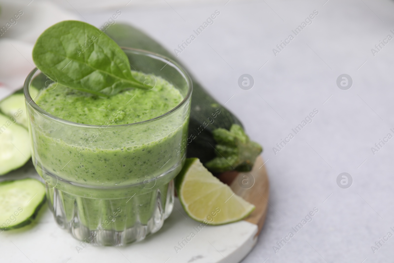 Photo of Tasty green smoothie in glass, lime and vegetables on light table, closeup. Space for text