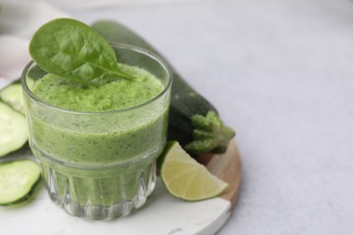 Photo of Tasty green smoothie in glass, lime and vegetables on light table, closeup. Space for text