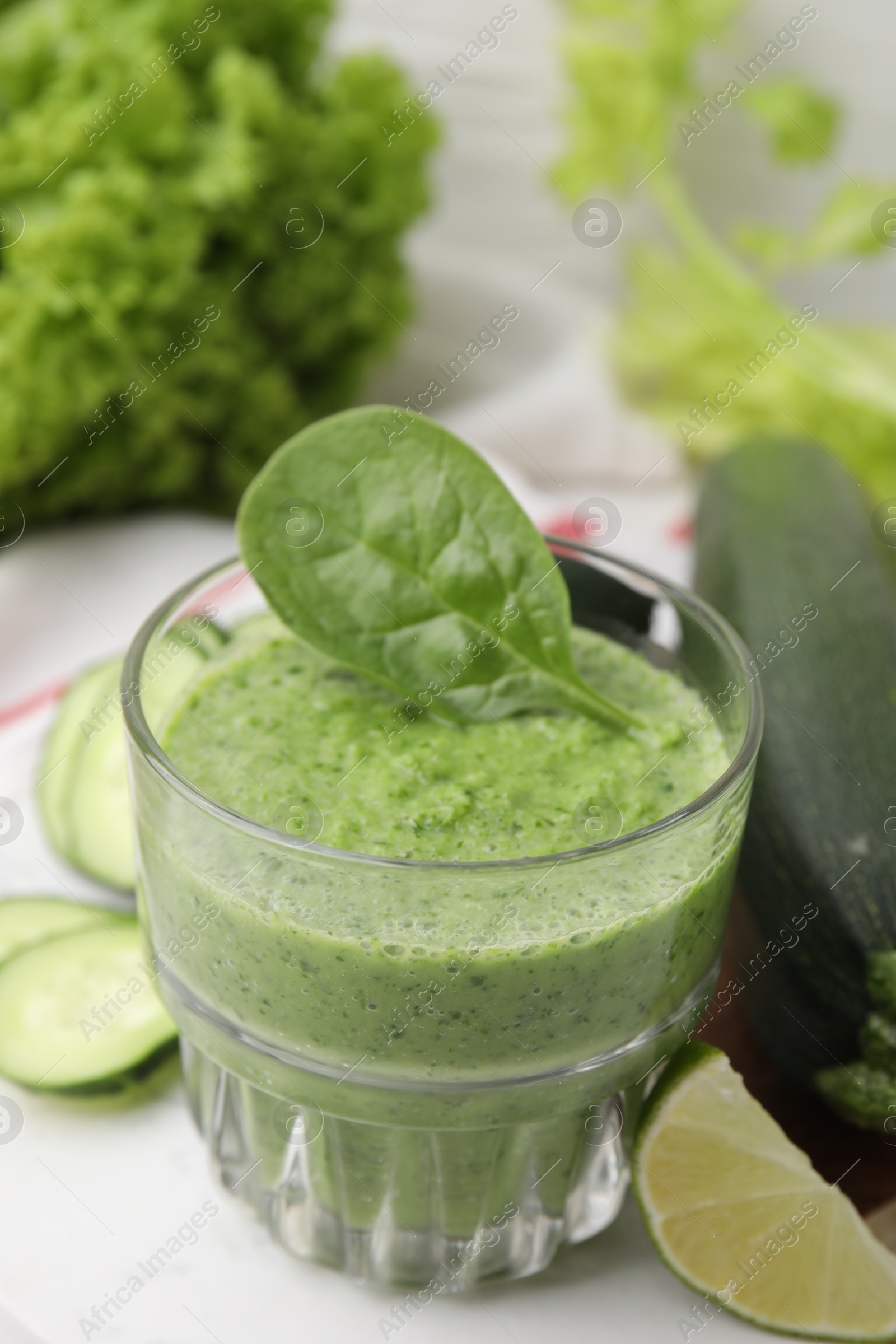 Photo of Tasty green smoothie in glass, lime and vegetables on table, closeup