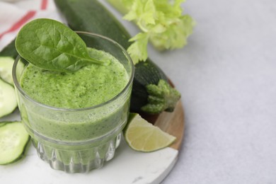 Photo of Tasty green smoothie in glass, lime and vegetables on light table, closeup. Space for text