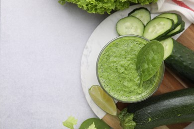 Photo of Tasty green smoothie in glass, lime and vegetables on light table, flat lay. Space for text