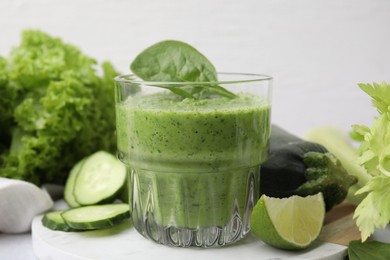 Photo of Tasty green smoothie in glass, lime and vegetables on table, closeup