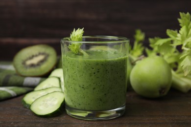 Tasty green smoothie in glass and cut cucumber on wooden table, closeup