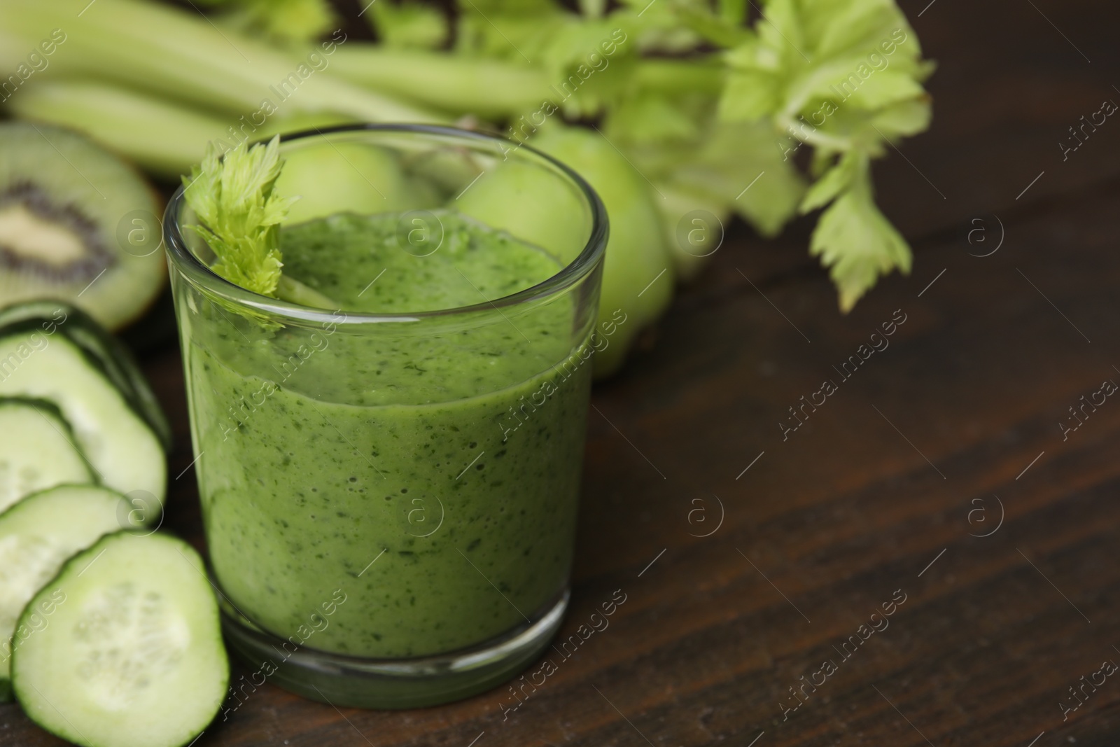 Photo of Tasty green smoothie in glass and cut cucumber on wooden table, closeup. Space for text