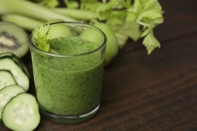 Photo of Tasty green smoothie in glass and cut cucumber on wooden table, closeup. Space for text