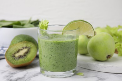 Tasty green smoothie in glass with lime and products on white marble table, closeup