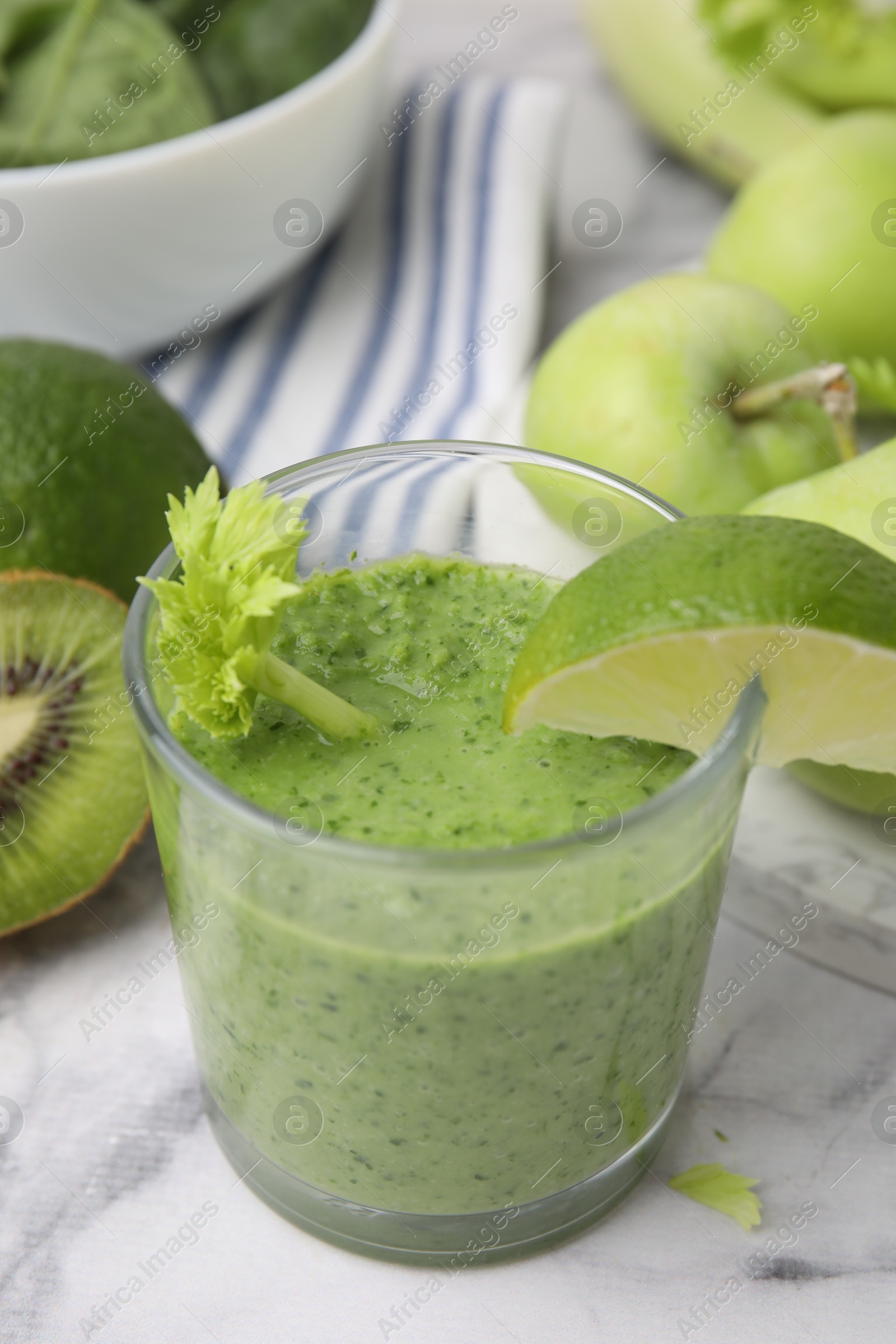 Photo of Tasty green smoothie in glass with lime and products on white marble table, closeup