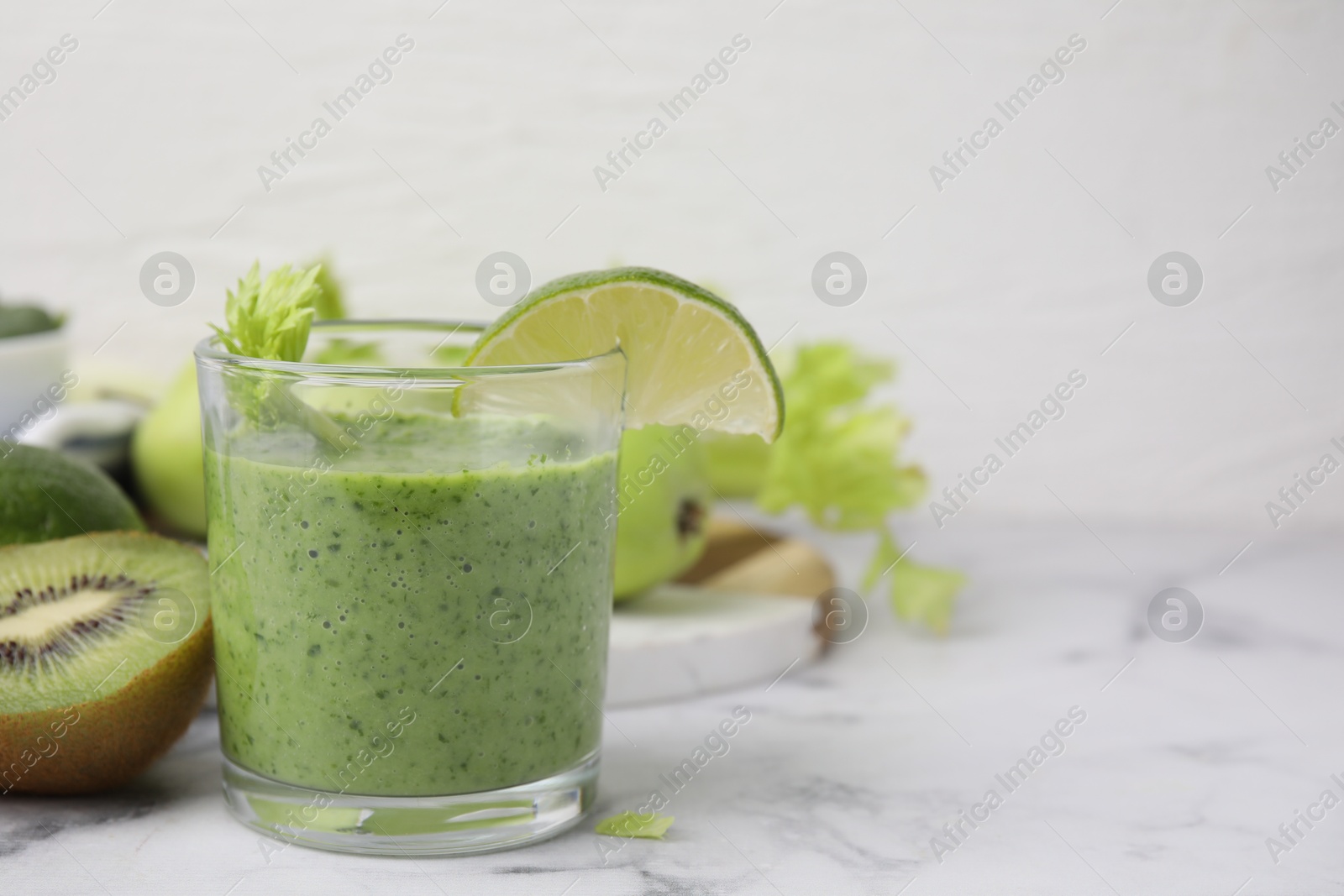 Photo of Tasty green smoothie in glass with lime and products on white marble table, closeup. Space for text