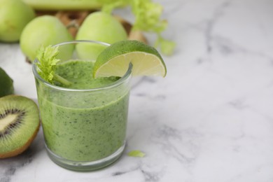 Photo of Tasty green smoothie in glass with lime and products on white marble table, closeup. Space for text