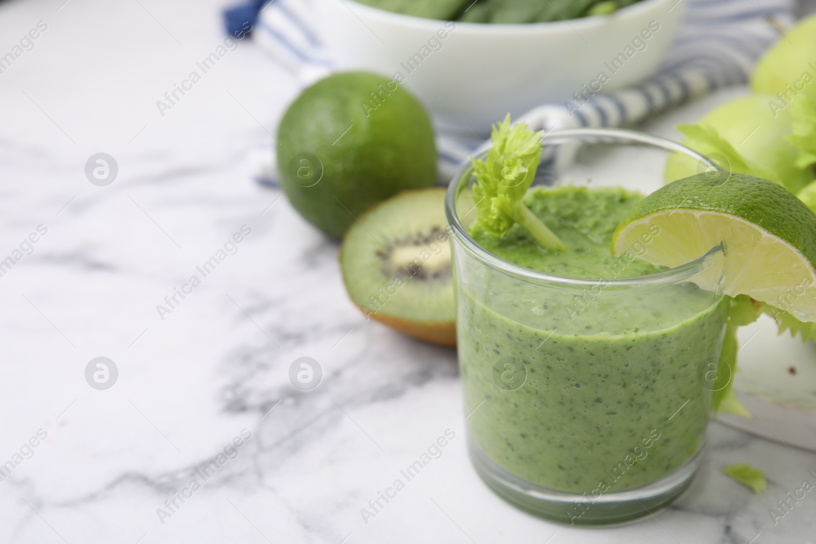 Photo of Tasty green smoothie in glass with lime and products on white marble table, closeup. Space for text