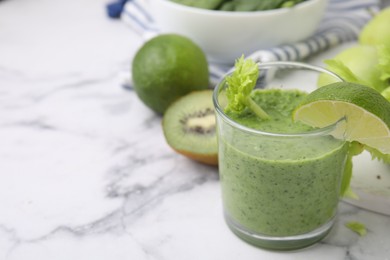 Photo of Tasty green smoothie in glass with lime and products on white marble table, closeup. Space for text