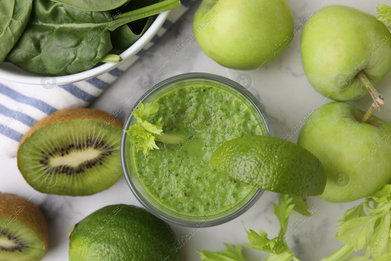 Photo of Tasty green smoothie in glass with lime and products on white marble table, flat lay