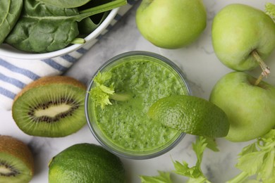 Tasty green smoothie in glass with lime and products on white marble table, flat lay