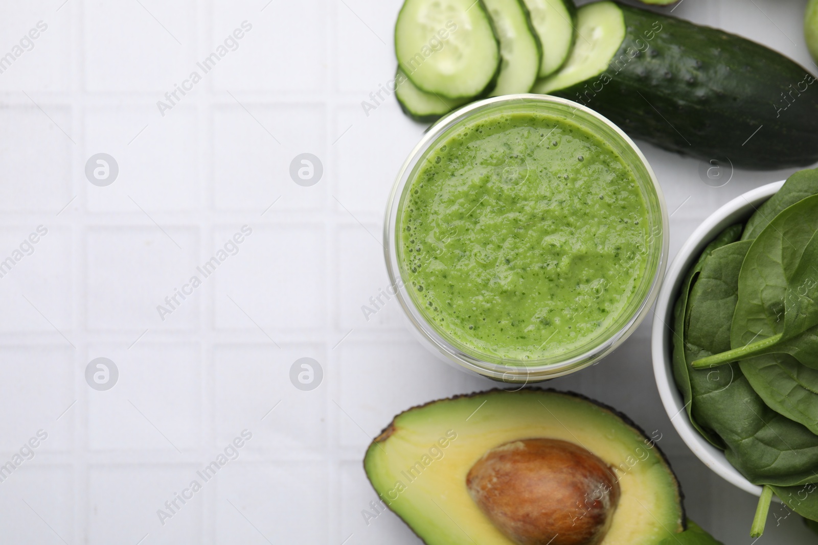 Photo of Tasty green smoothie in glass and products on white tiled table, flat lay. Space for text